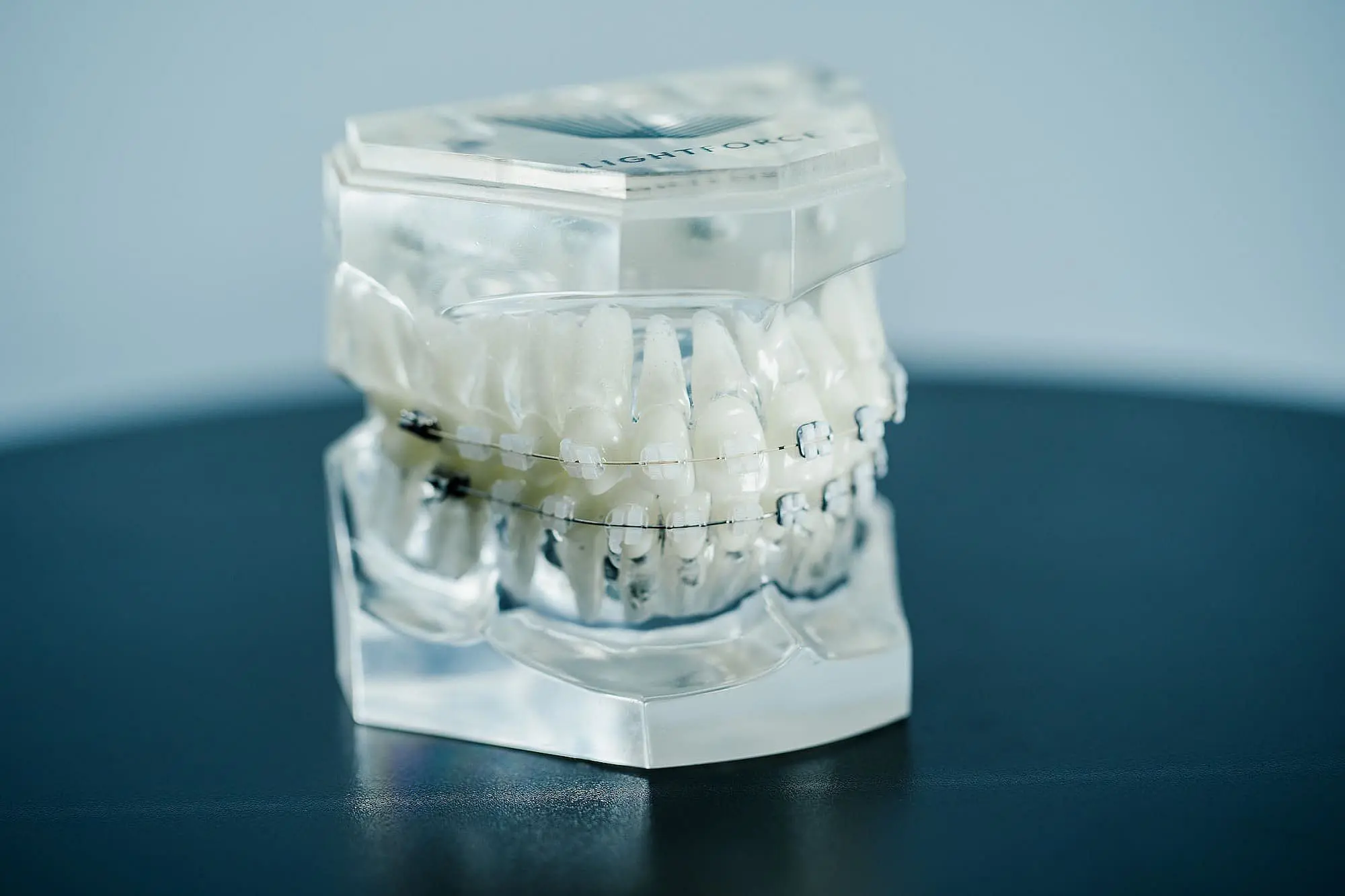 A transparent dental model showcasing a full set of human teeth adorned with LightForce braces, positioned elegantly on a dark surface in Leominster or Gardner, MA