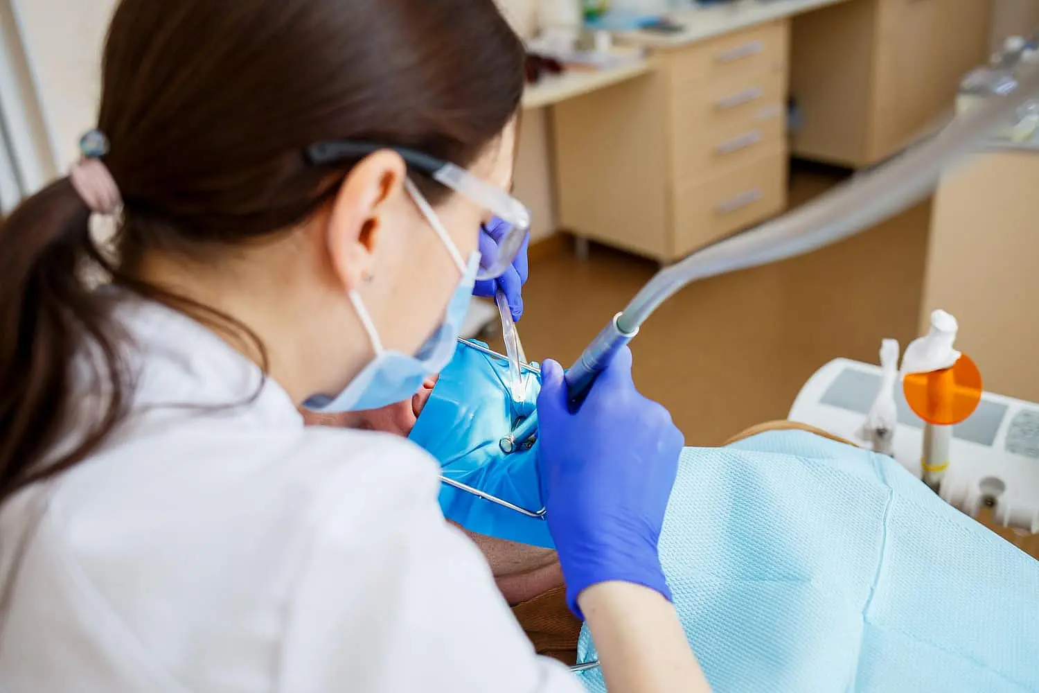 A dentist in gloves and protective eyewear carefully addresses a dental procedure on a patient with tongue thrust tendencies in the clinic in Leominster and Gardner, MA