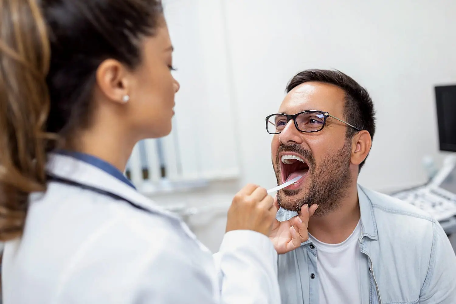 A healthcare professional examines a man's throat with a tongue depressor, checking for signs of tongue thrust while ensuring a thorough evaluation in Leominster and Gardner, MA