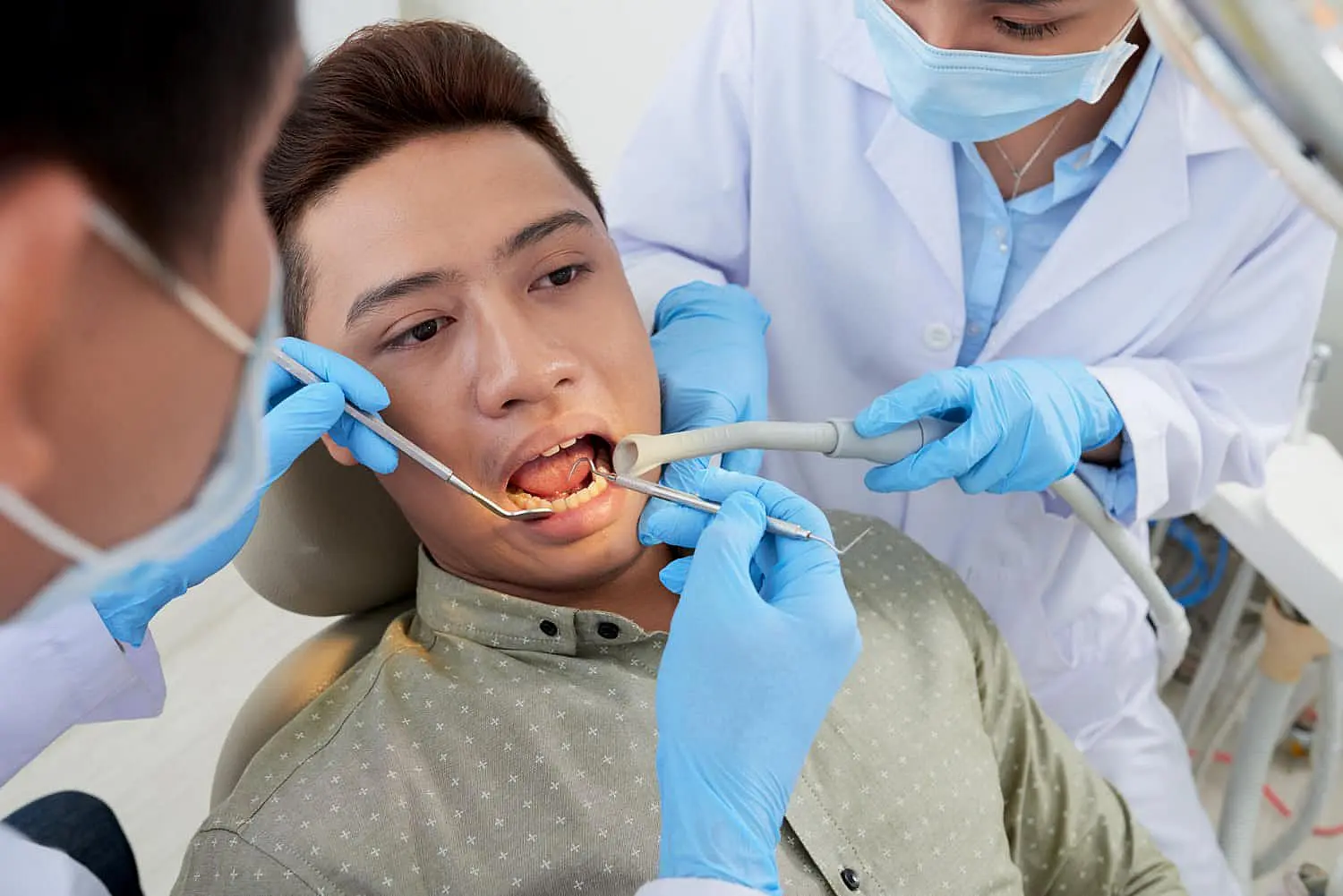 A patient with tongue thrust receives dental treatment in a clinic. Two dentists in masks and gloves work diligently on his teeth using specialized tools in Leominster and Gardner, MA