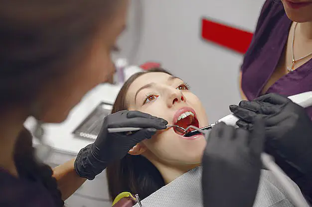 A woman is lying back in a dental chair with her mouth open, possibly indicating issues like tongue thrust, as two gloved individuals evaluate her teeth using dental tools in Leominster and Gardner, MA