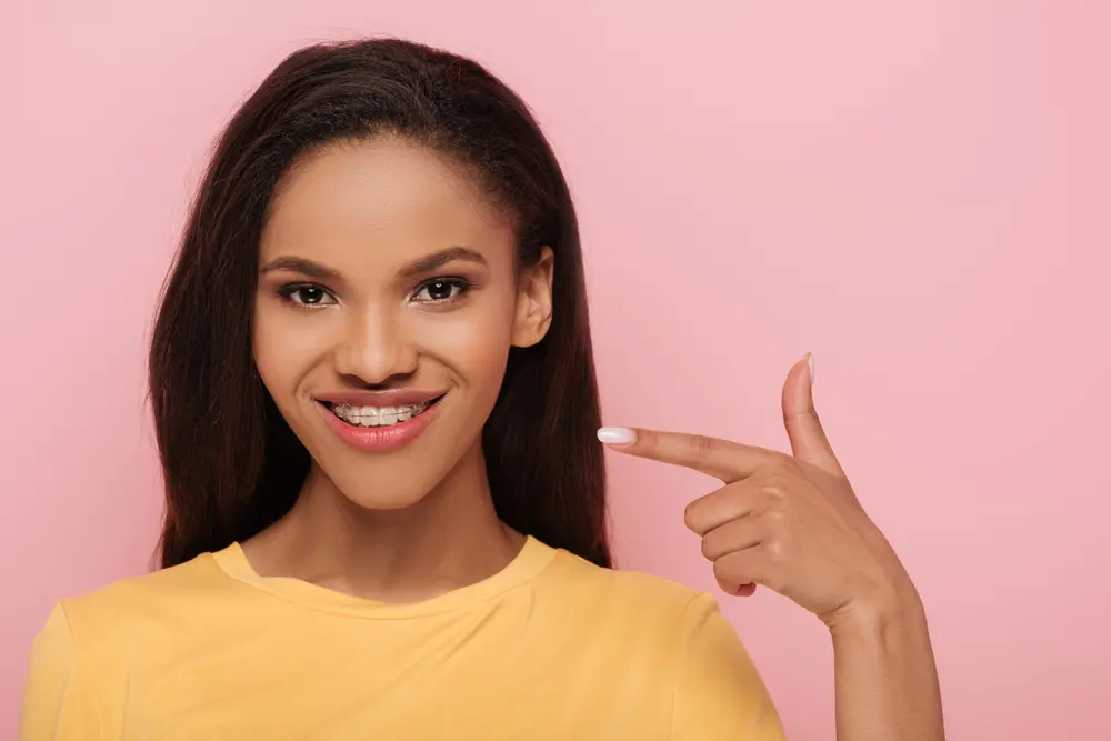 smiling african american girl pointing finger metal braces her teeth - Alternatives to Braces in Leominster and Gardner, MA.
