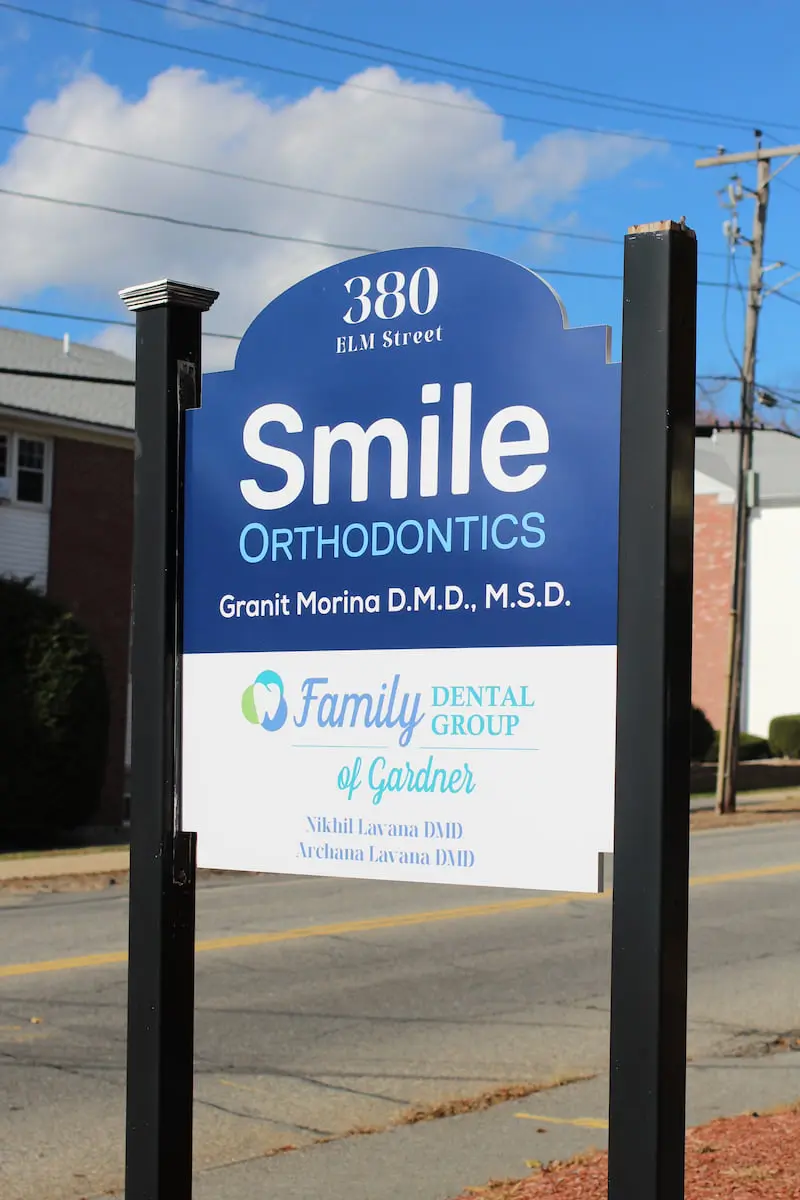 Smile Orthodontics in Gardner, MA, has a street sign at 380 Elm Street displaying the names of dentists Granit Morina, Nikhil Lavana, and Archana Lavana—your trusted local orthodontic team.