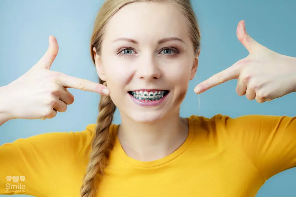 a woman pointing at her metal braces after understanding about how long do braces take in leominster and gardner, ma