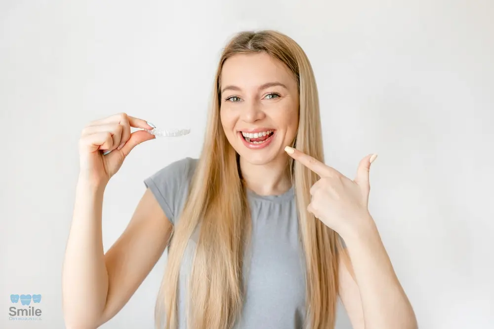 Happy woman pointing at clear aligners in her hand, showcasing Invisalign treatment results after understanding about Does Insurance Cover Invisalign Leominster and Gardner, MA.