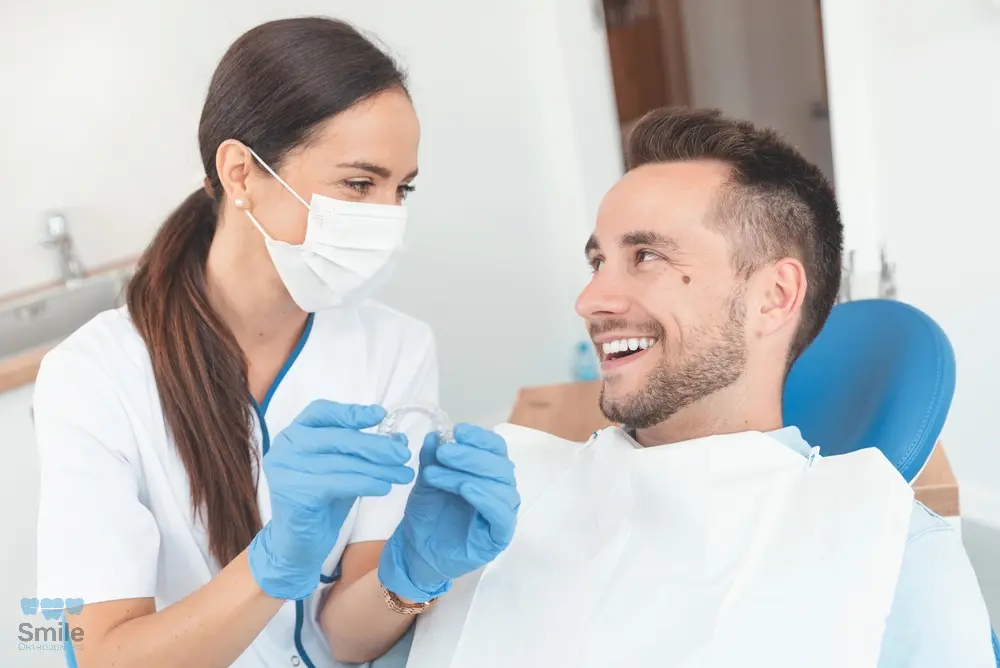 Female dentist showing clear aligners to a smiling male patient during an orthodontic consultation while explaining about Does Insurance Cover Invisalign Leominster and Gardner, MA.
