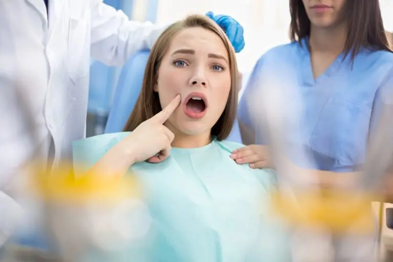 Girl sitting in a dental chair pointing at her teeth while talking to a dentist - Overbite vs Underbite in Leominster and Gardner, MA.
