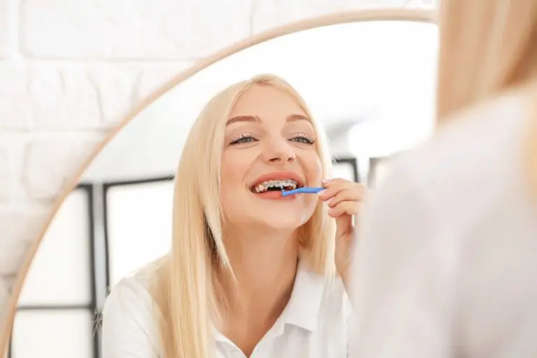 young woman metal braces toothbrush home - How to Floss with Braces in Leominster and Gardner, MA