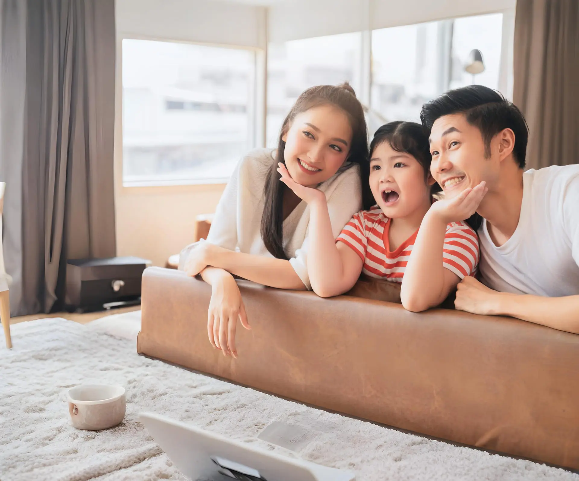 Inside a well-lit room at Smile Orthodontics in Gardner, MA, two adults and a child smile together while leaning on the back of a couch and gazing in the same direction.